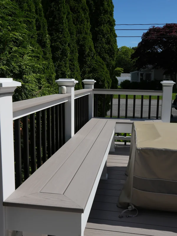 Deck railing with built-in seating and green privacy trees