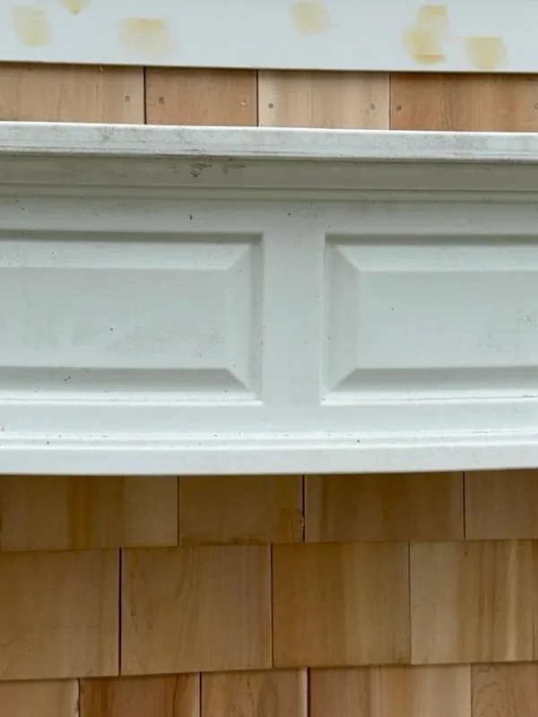 White exterior trim detail below cedar shingle siding