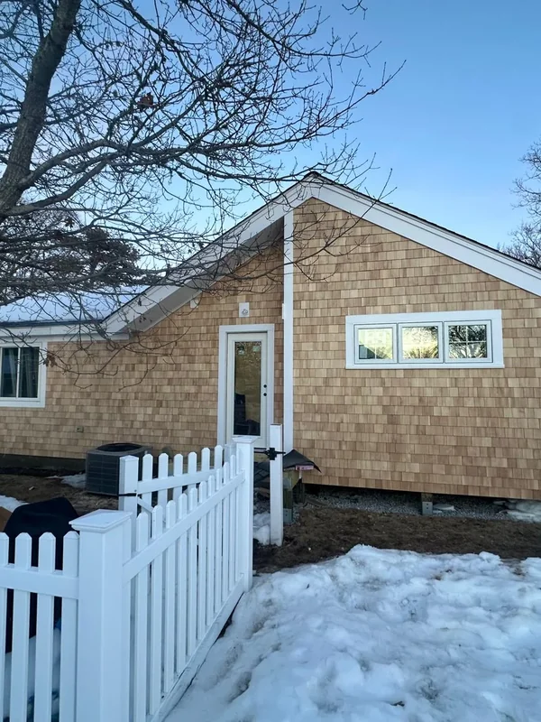 Rear exterior with cedar siding, windows, and white fence